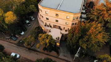 An aerial view of a multi-story building with a courtyard, surrounded by trees and parked cars.