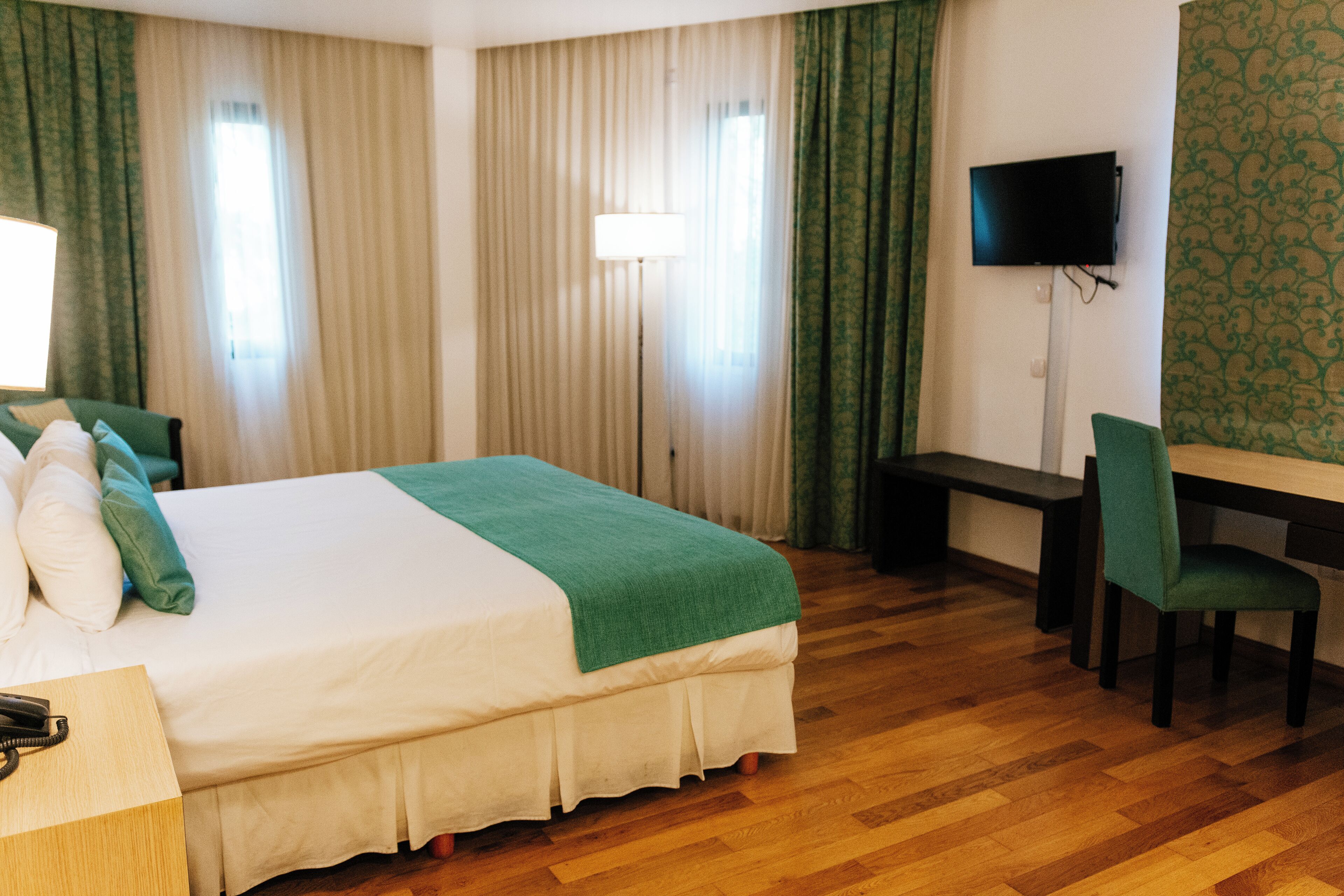A hotel room with a bed, a desk, a chair, a television, and a telephone.