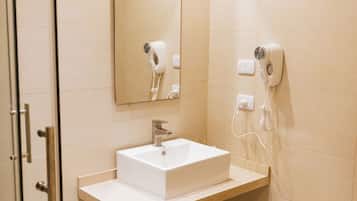 Un bagno moderno con una cabina doccia in vetro, un lavandino bianco e uno specchio sopra. Due asciugacapelli sono montati a parete.