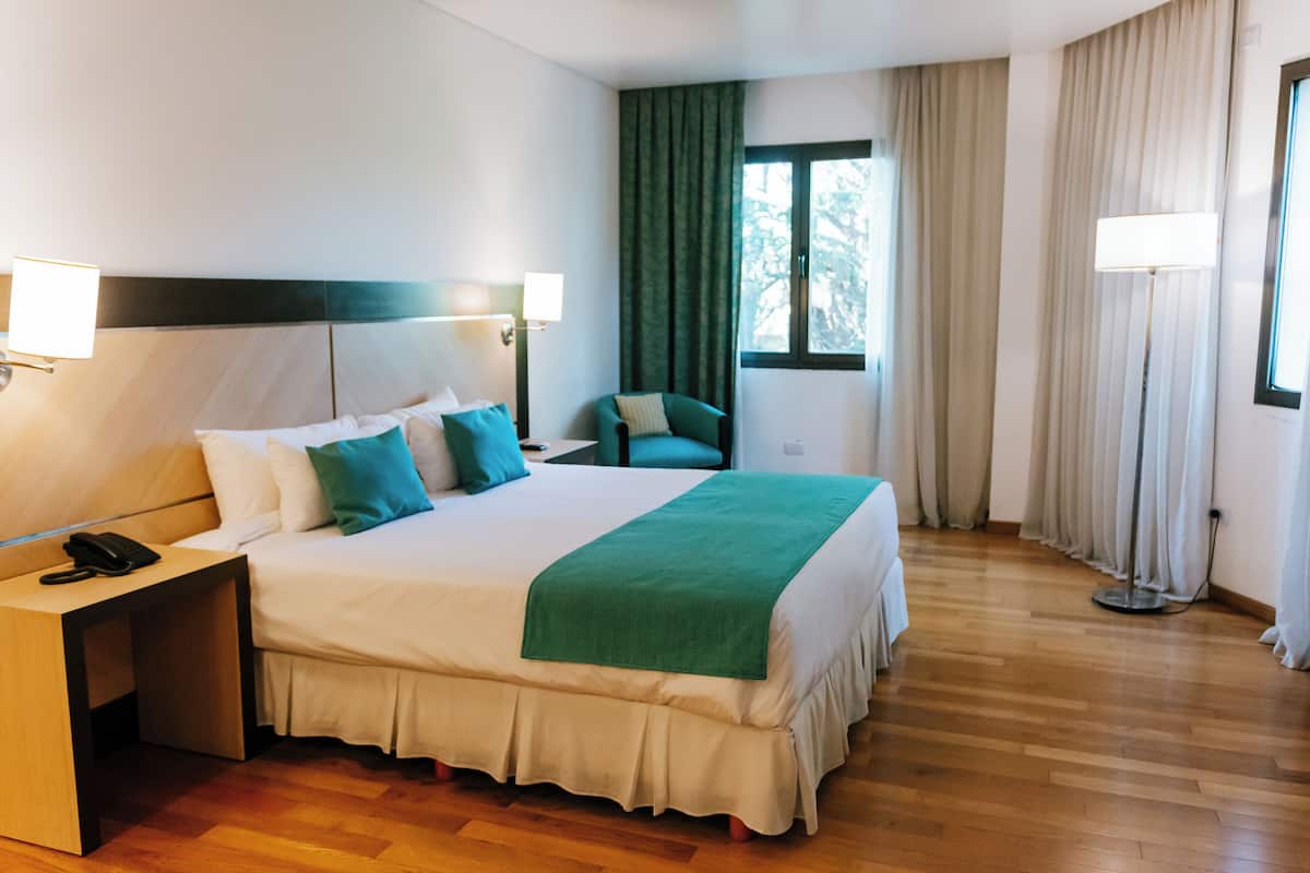 Una habitación de hotel con una cama grande, lámparas de noche, un escritorio con teléfono y una silla.
