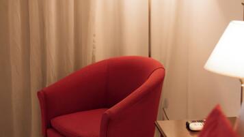 A hotel room with a red armchair, a bedside table with a lamp, and a bed.