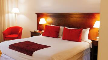 A neatly made bed with red and white pillows, a wooden headboard, and a red chair beside it.