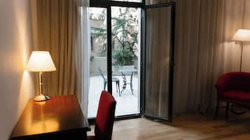 Una habitación con una mesa de madera, una silla roja, una lámpara y un ventanal corredero que da a un espacio exterior con una mesa y sillas.