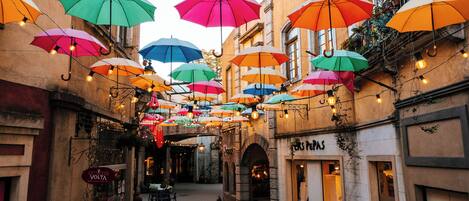 Une rue étroite, au-dessus de laquelle sont suspendus des parasols colorés, créant une ambiance animée.