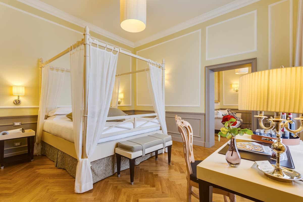 A four-poster canopy bed with a bench, bedside table, and lamp.
