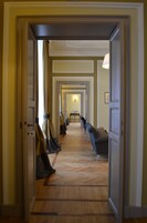Un corridoio con porte su entrambi i lati, che conduce a una stanza con un letto e una poltrona.