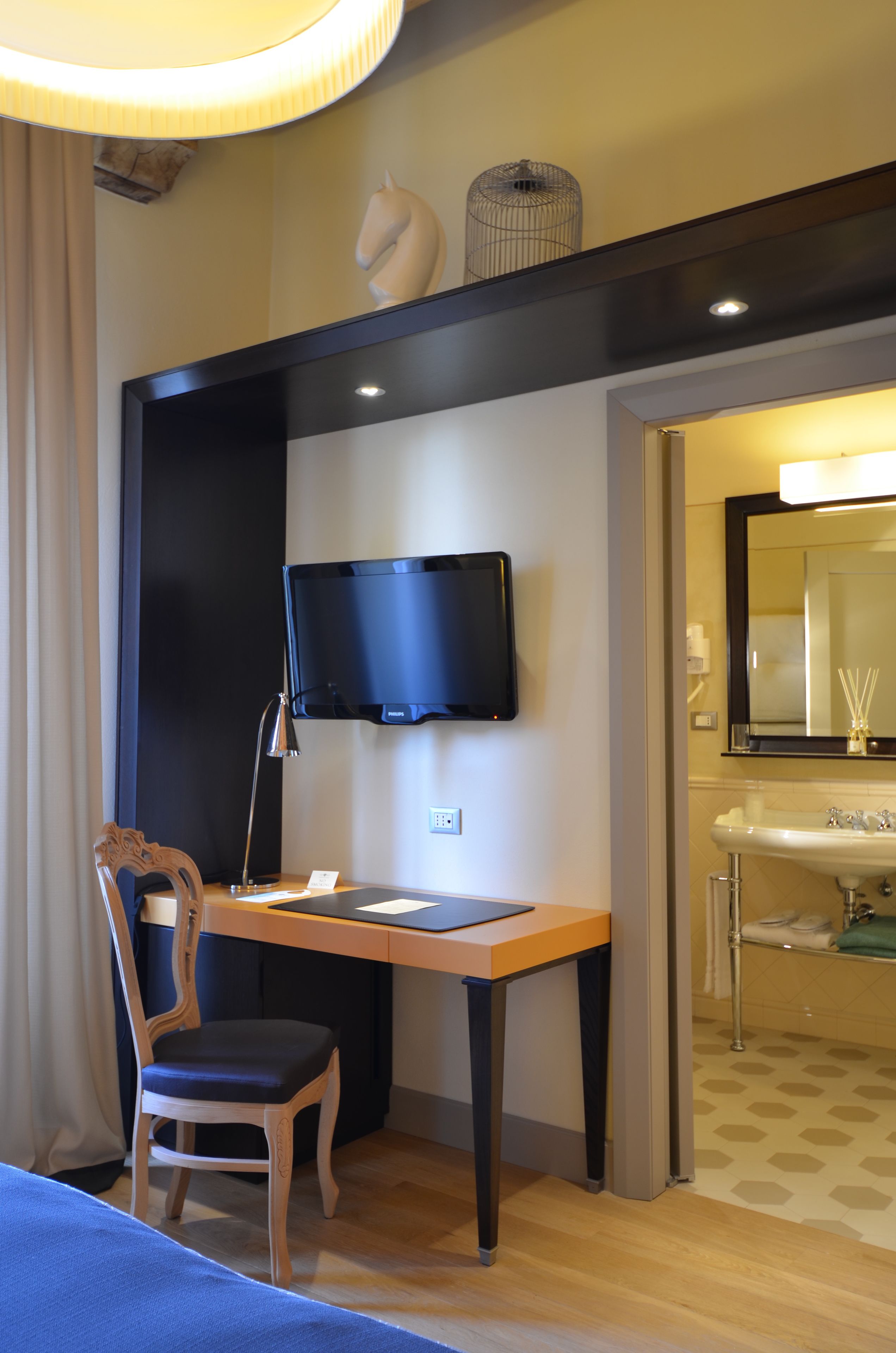 Una habitación de hotel con escritorio, silla, televisión y baño con lavamanos y espejo.