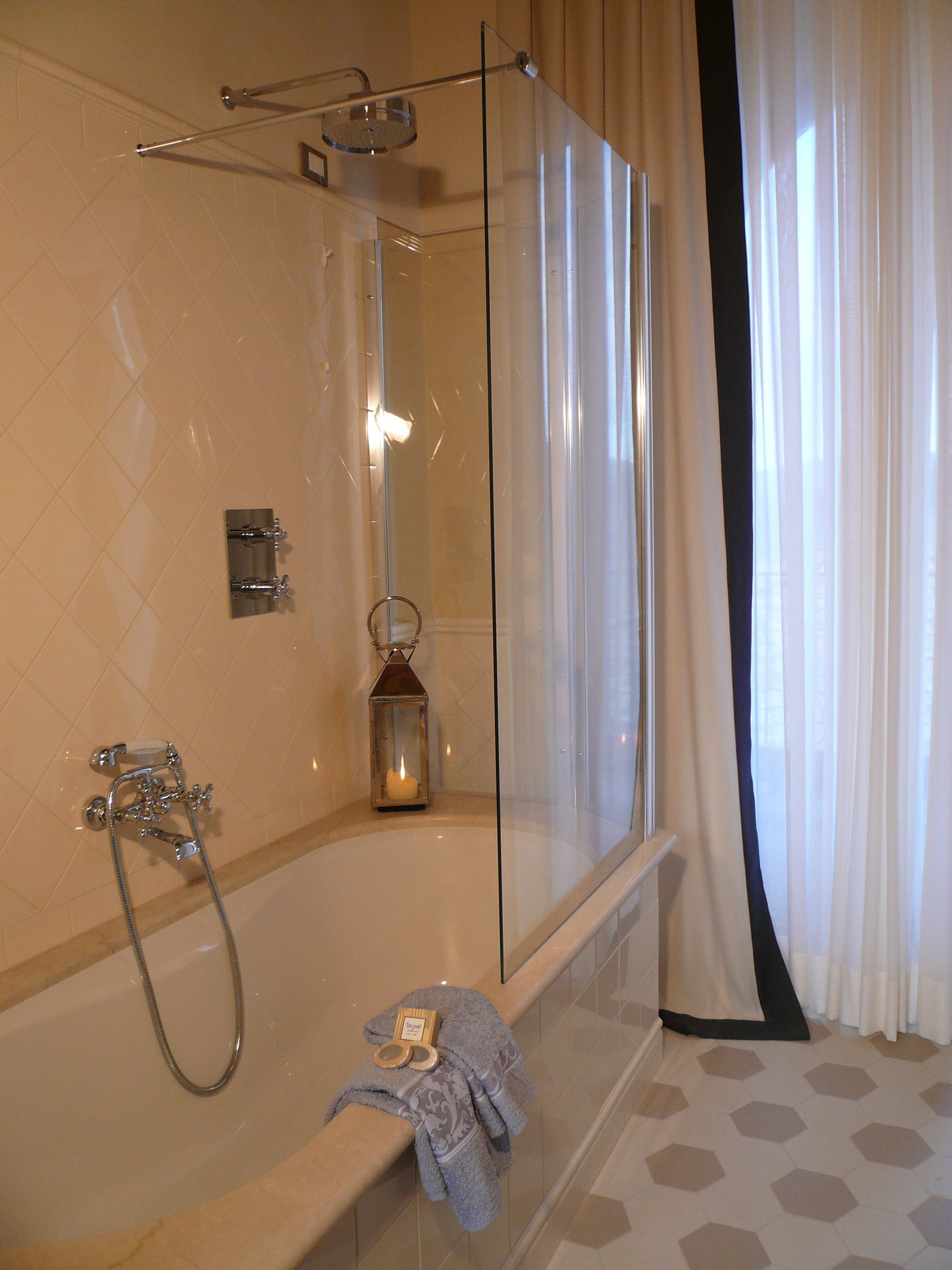 A modern bathroom with a glass-enclosed shower, a bathtub with a towel and bath products, and a candle on the edge.