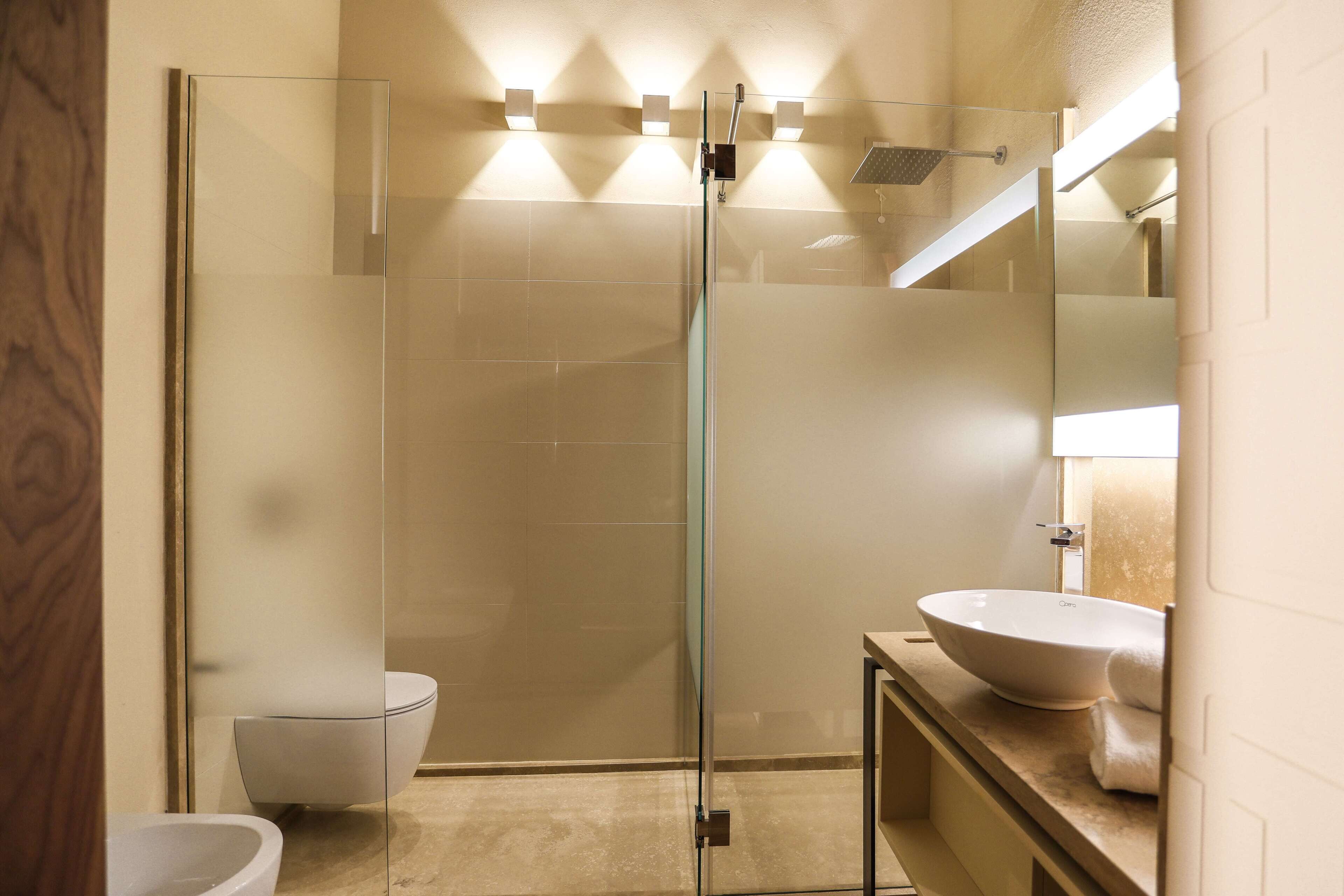 Un baño moderno con ducha envuelta en vidrio, inodoro blanco y un lavamanos grande tipo recipiente.