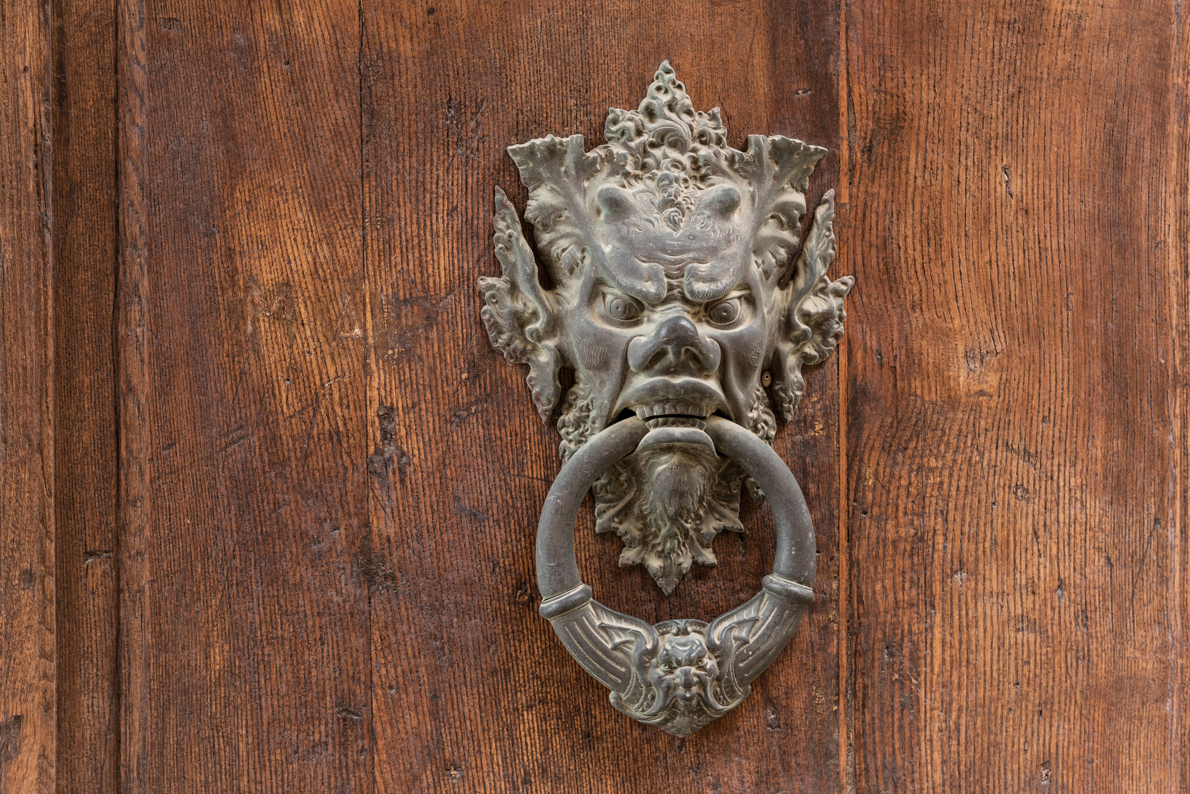 Um bate-porta de metal com um desenho ornamentado numa porta de madeira.