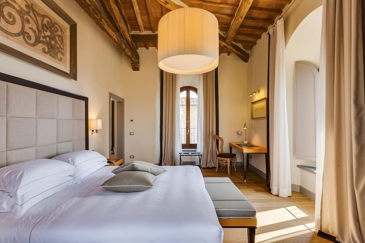 A hotel room with a large bed, a desk, a chair, and a hanging light fixture.