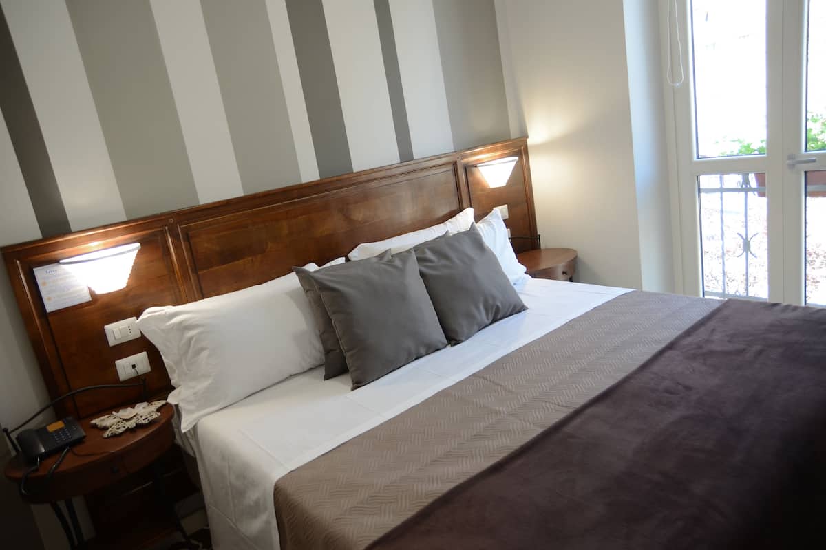 A neatly made bed with a wooden headboard, white and gray pillows, and a brown blanket. There is a bedside table with a phone and a decorative item.