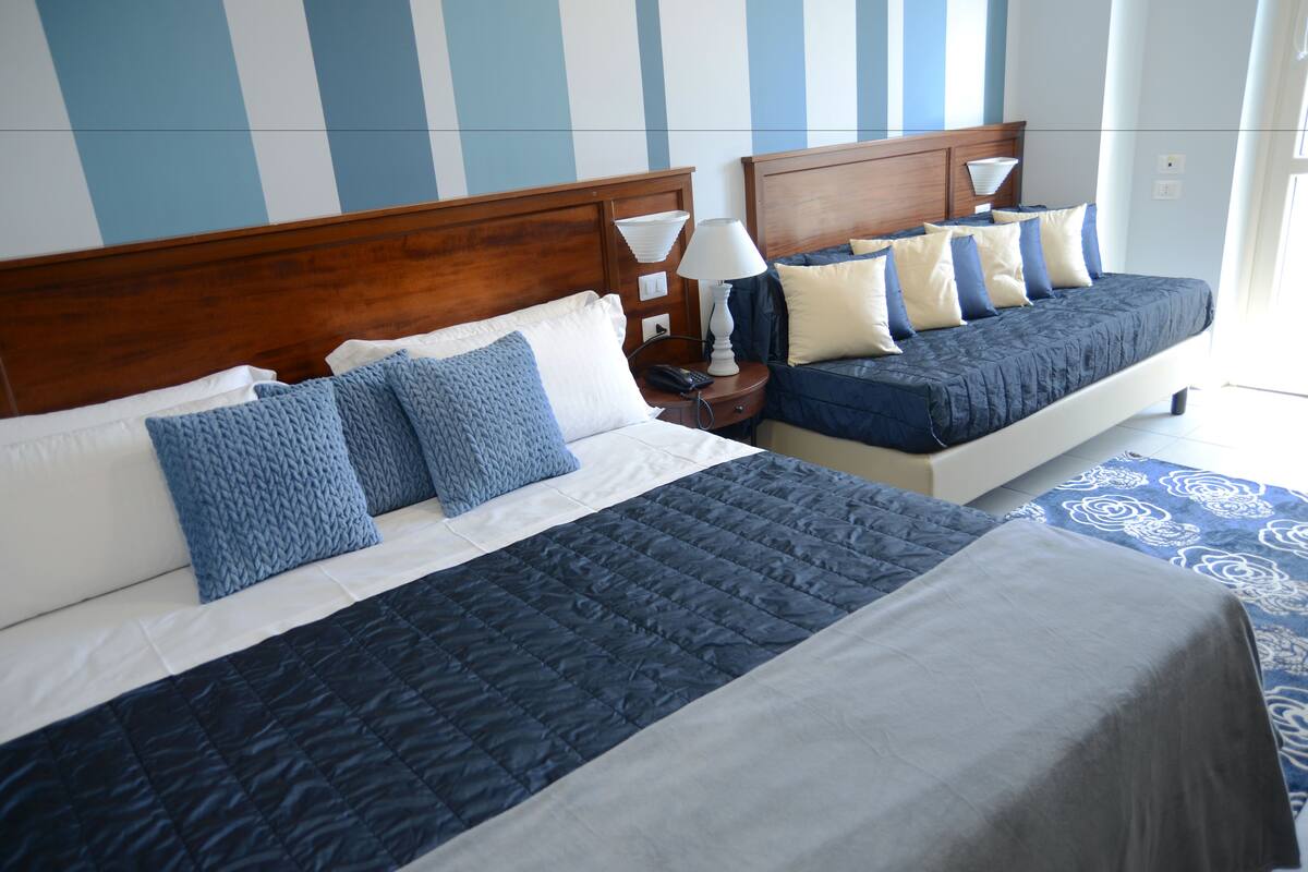 Two double beds with wooden headboards, white nightstands, and a blue and white striped wall.