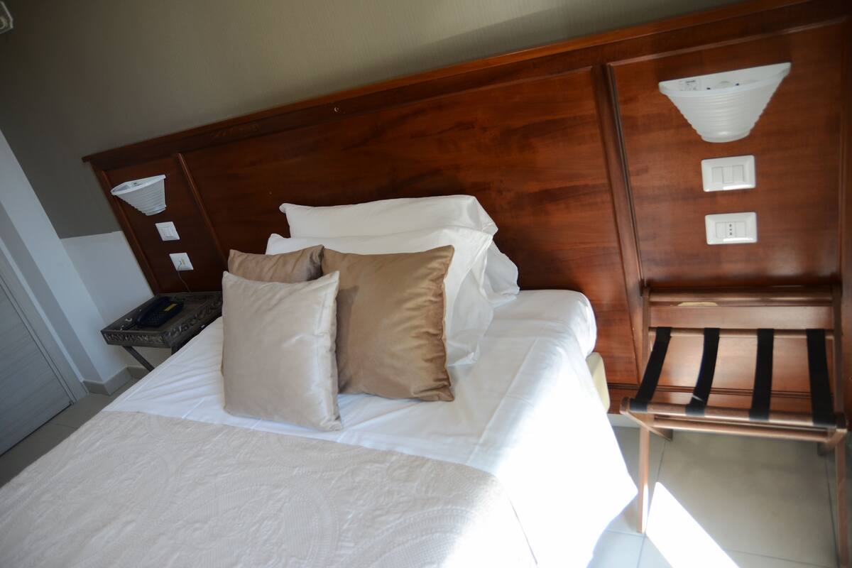 A neatly made bed with white and beige linens, a wooden headboard, and a bedside table with a lamp.
