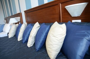 Una cama bien hecha con un edredón oscuro y una hilera de almohadas en azul y beige.