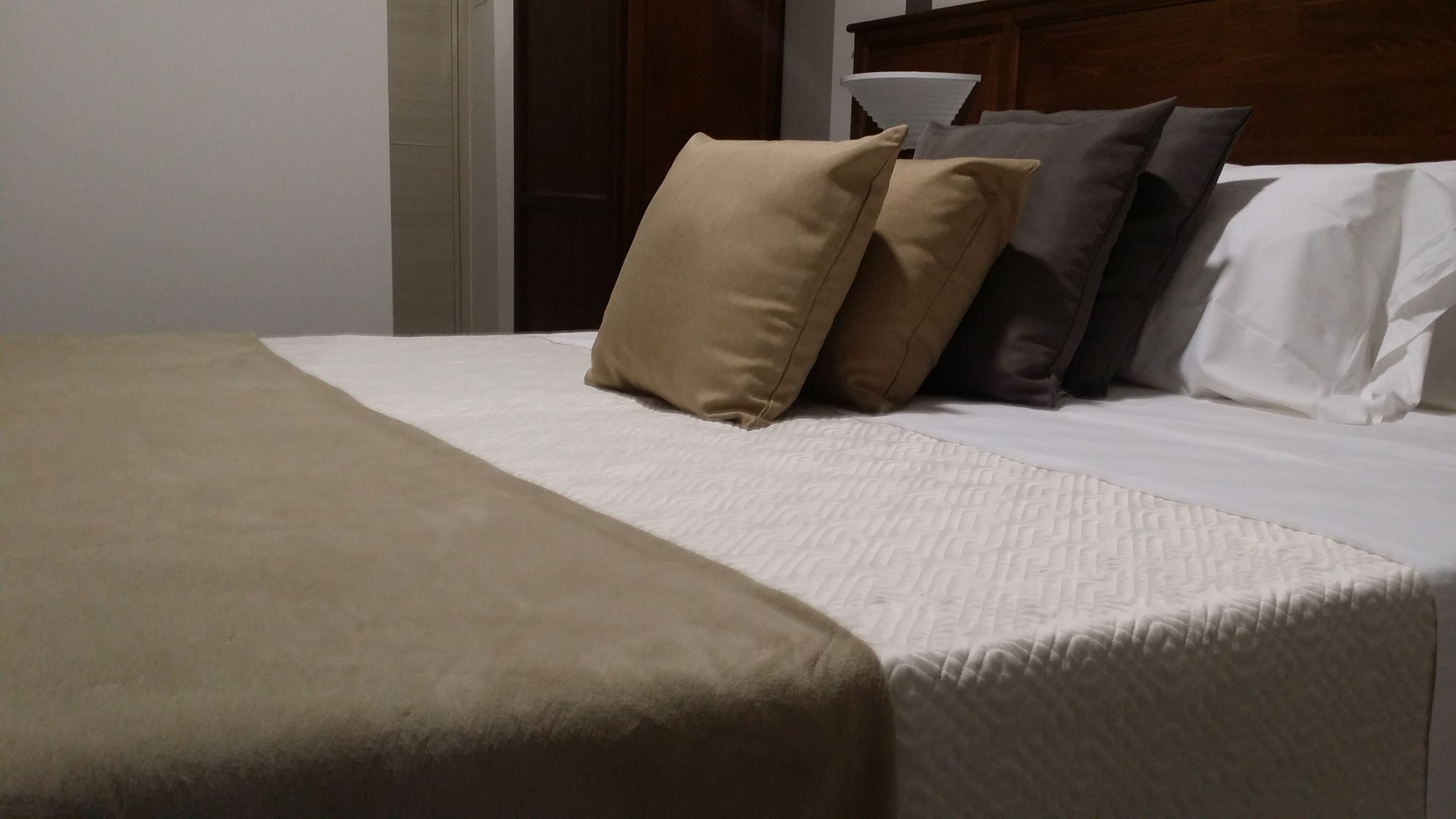 Una cama bien hecha con una colcha color beige y almohadas, un cabecero de madera y una pared blanca.