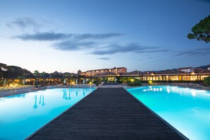 Ein Pool mit Holzterrasse, umgeben von Gebäuden mit warmer Beleuchtung.