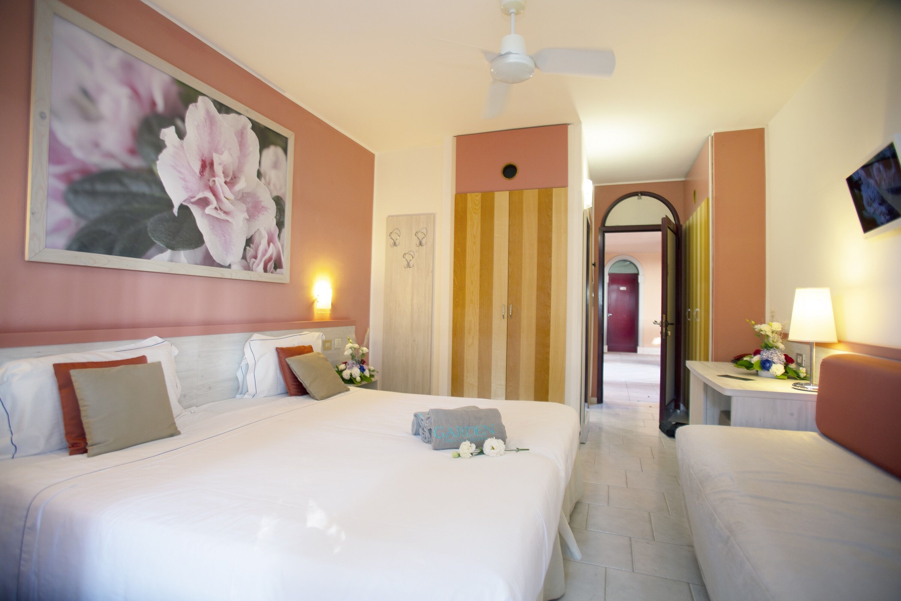 A hotel room with a large bed, a bedside table with a lamp, a painting on the wall, and a door leading to another room.