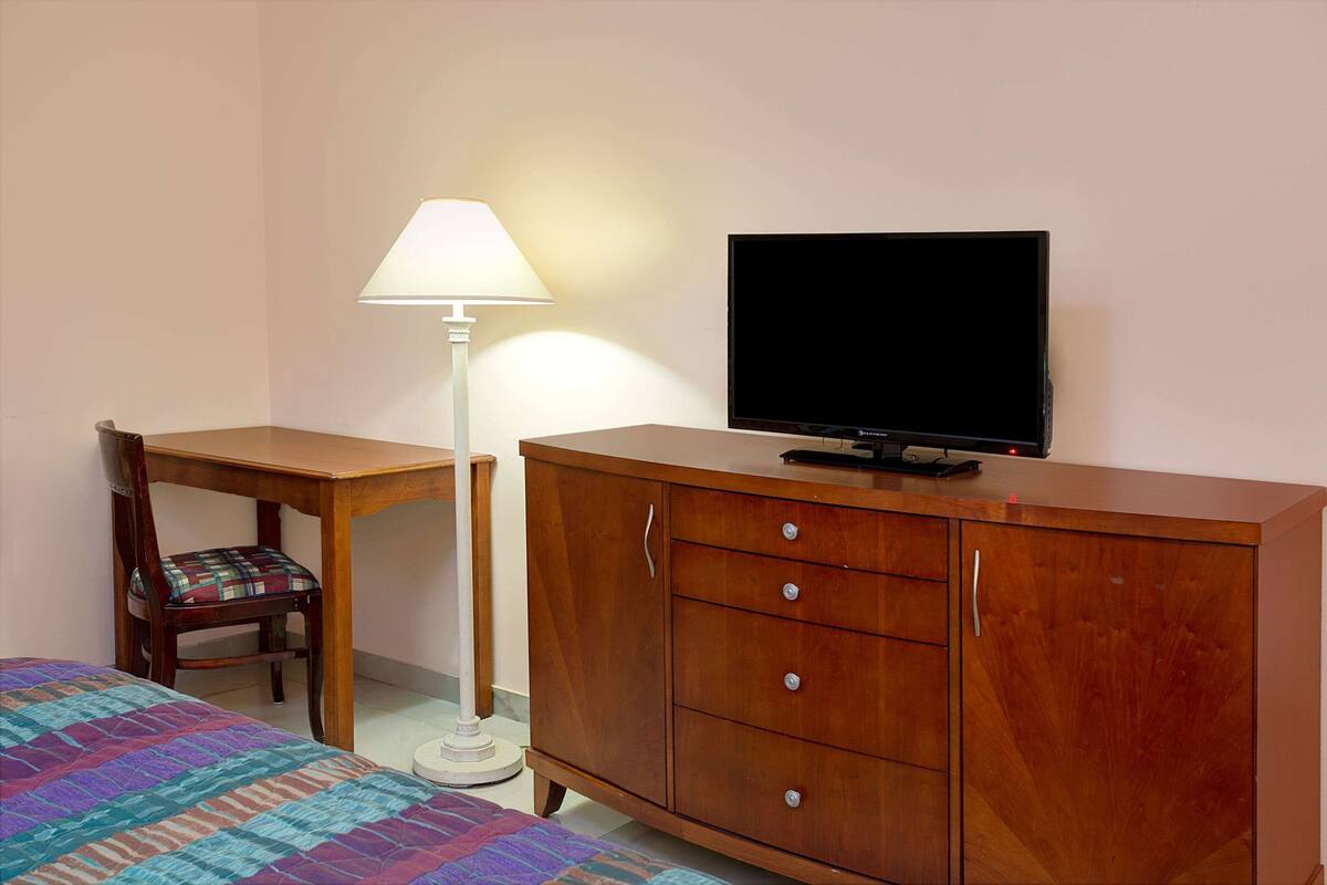 A room with a bed, a desk, a chair, a television, and a cabinet.
