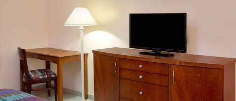 Una habitación con cama, escritorio, silla, televisor y armario.