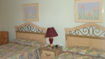 A bedroom with two beds, a nightstand, a lamp, and two framed pictures on the wall.