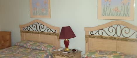 A bedroom with two beds, a nightstand, a lamp, and two framed pictures on the wall.