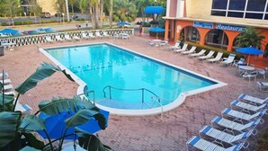 A swimming pool with lounge chairs and umbrellas, surrounded by a brick patio.