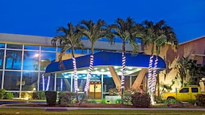 A building with a blue awning, palm trees, and a yellow vehicle in front.