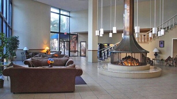 A spacious lobby with a central fireplace, comfortable seating, and a staircase leading to upper floors.