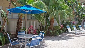 A patio area with a round table and chairs, a blue umbrella, and lounge chairs.