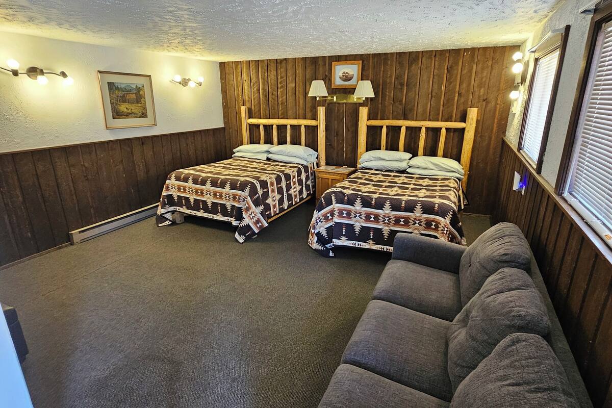 A room with two beds, a sofa, wooden walls, and a ceiling with a textured finish.