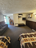 A room with a sofa, a bed with patterned bedding, a small table with a chair, a microwave, and a television mounted on the wall.