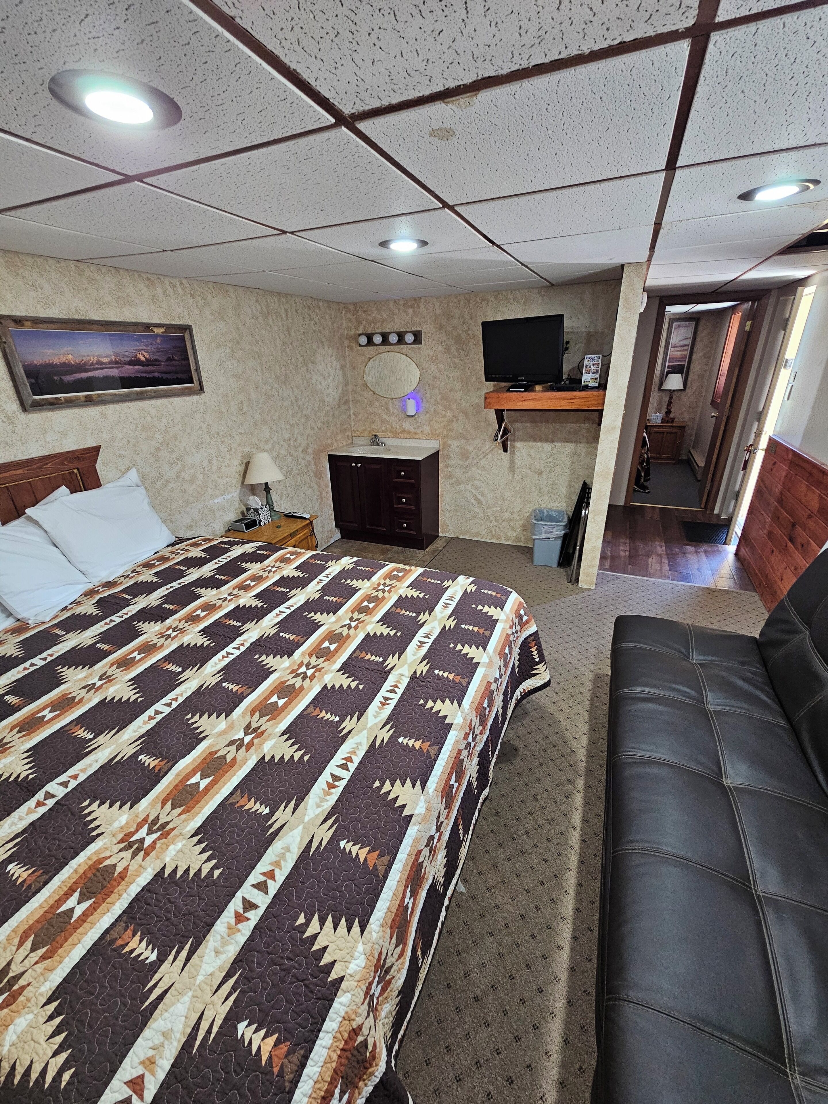 Hotelkamer met een bed, een slaapbank, een televisie, een bureau en een zichtbare badkamer door een open deur.