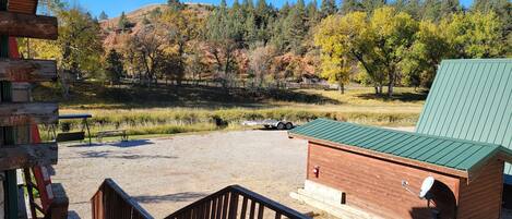 A rustic cabin with a green roof, a gravel driveway, and a wooden deck.
