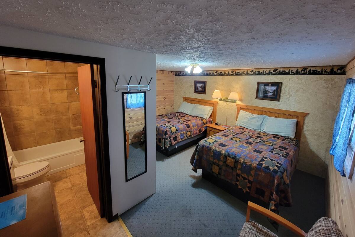 A hotel room with two beds, a bathroom, and a small seating area.