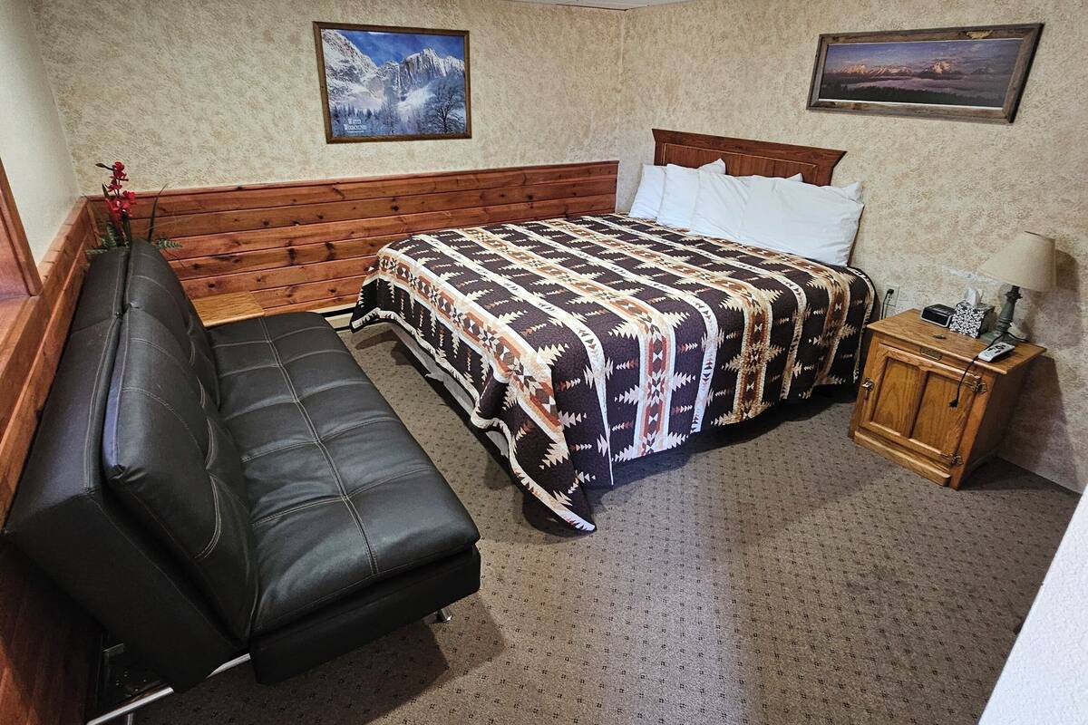 A bedroom with a bed, a wooden bench, a nightstand, and two framed pictures on the wall.