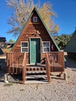 A small wooden cabin with a green door, two windows, and a porch with steps leading to the entrance.