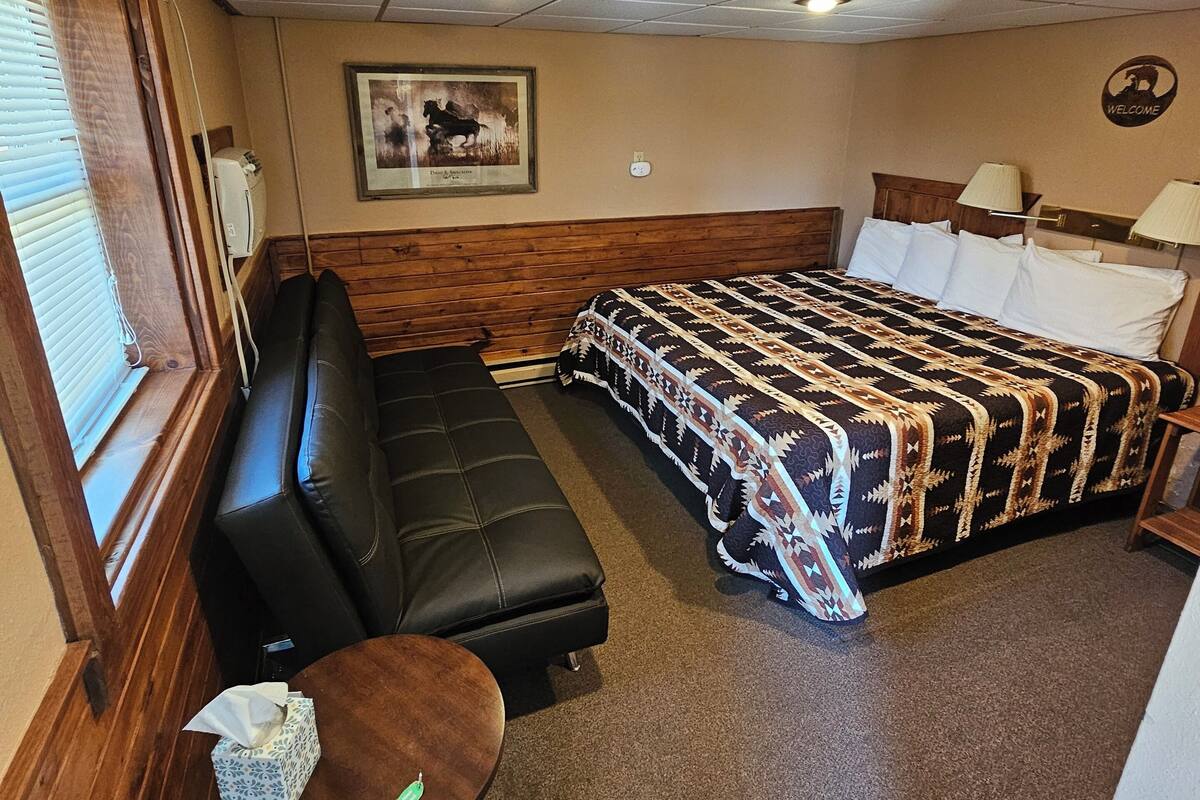A hotel room with a bed, a sofa, a small table, and a window.