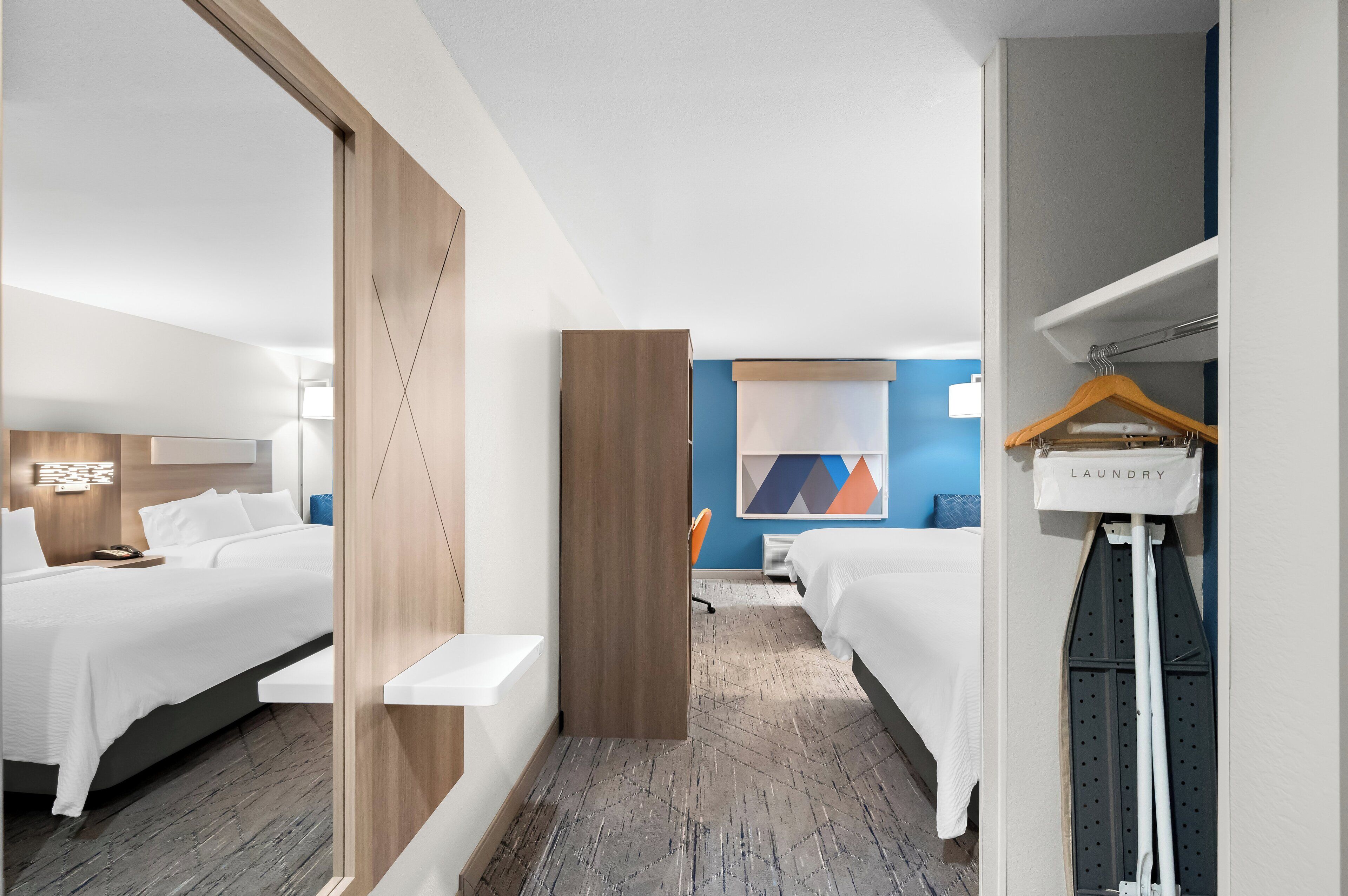 Een hotelkamer met twee bedden, een houten scheidingswand, een wasstation en een blauwe accentmuur.