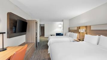 A hotel room with a flat-screen TV, two beds, a desk with a chair, and a small table with a lamp.