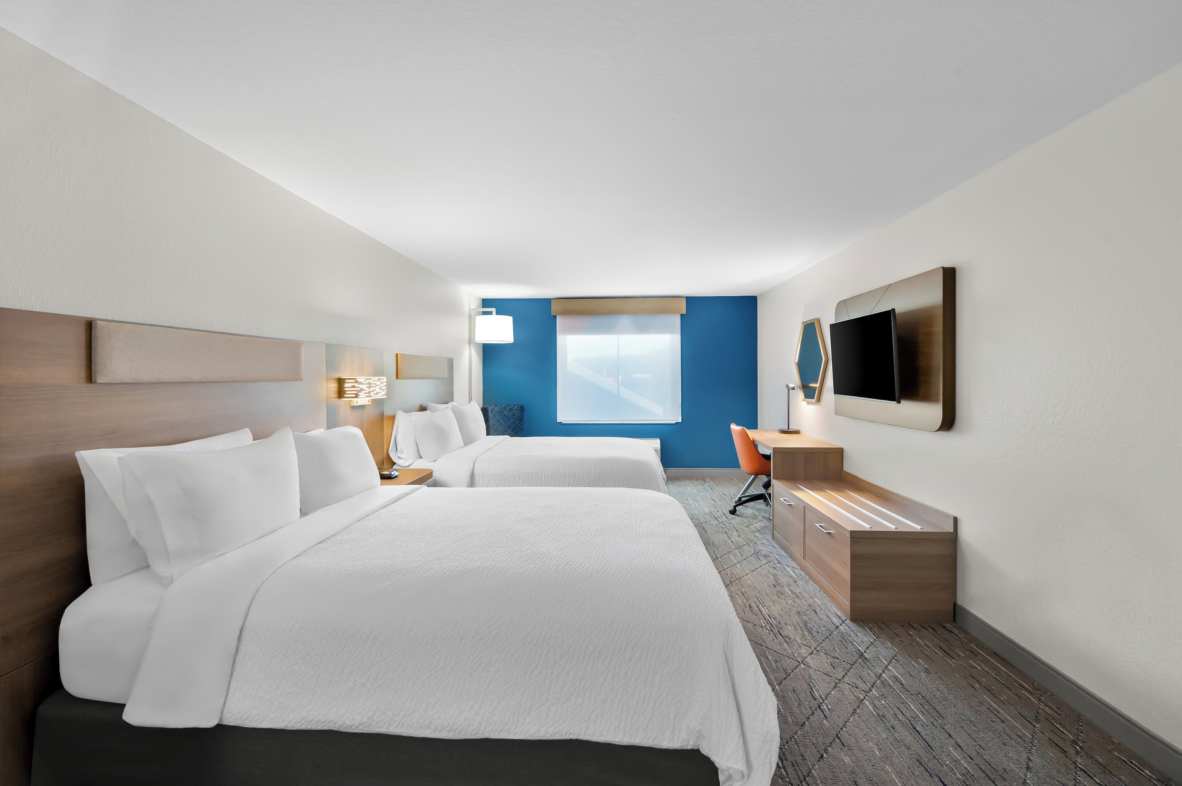 A hotel room with two beds, a desk, a TV, and a window with a view.