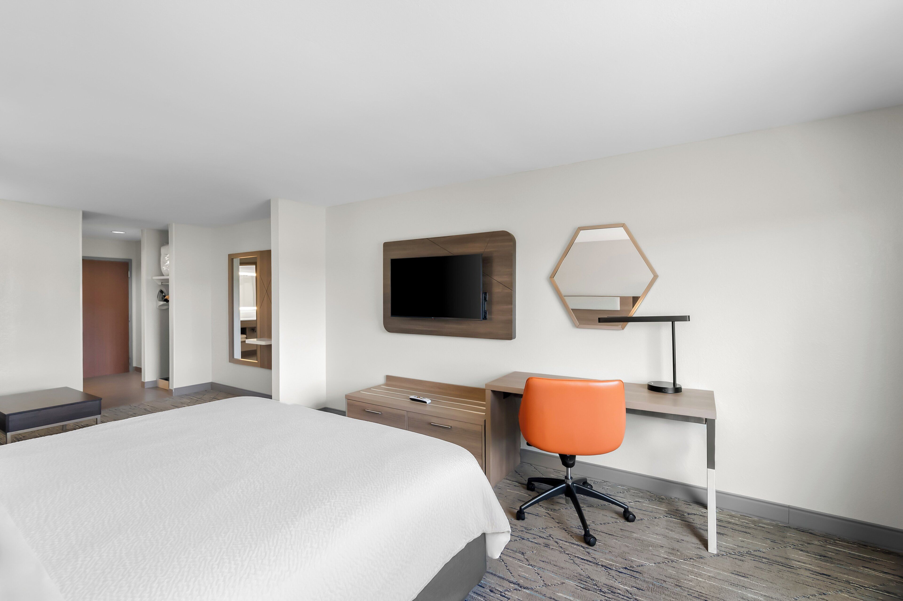 Ett hotellrum med en stor säng, ett skrivbord med en stol, en platt-TV och en spegel.