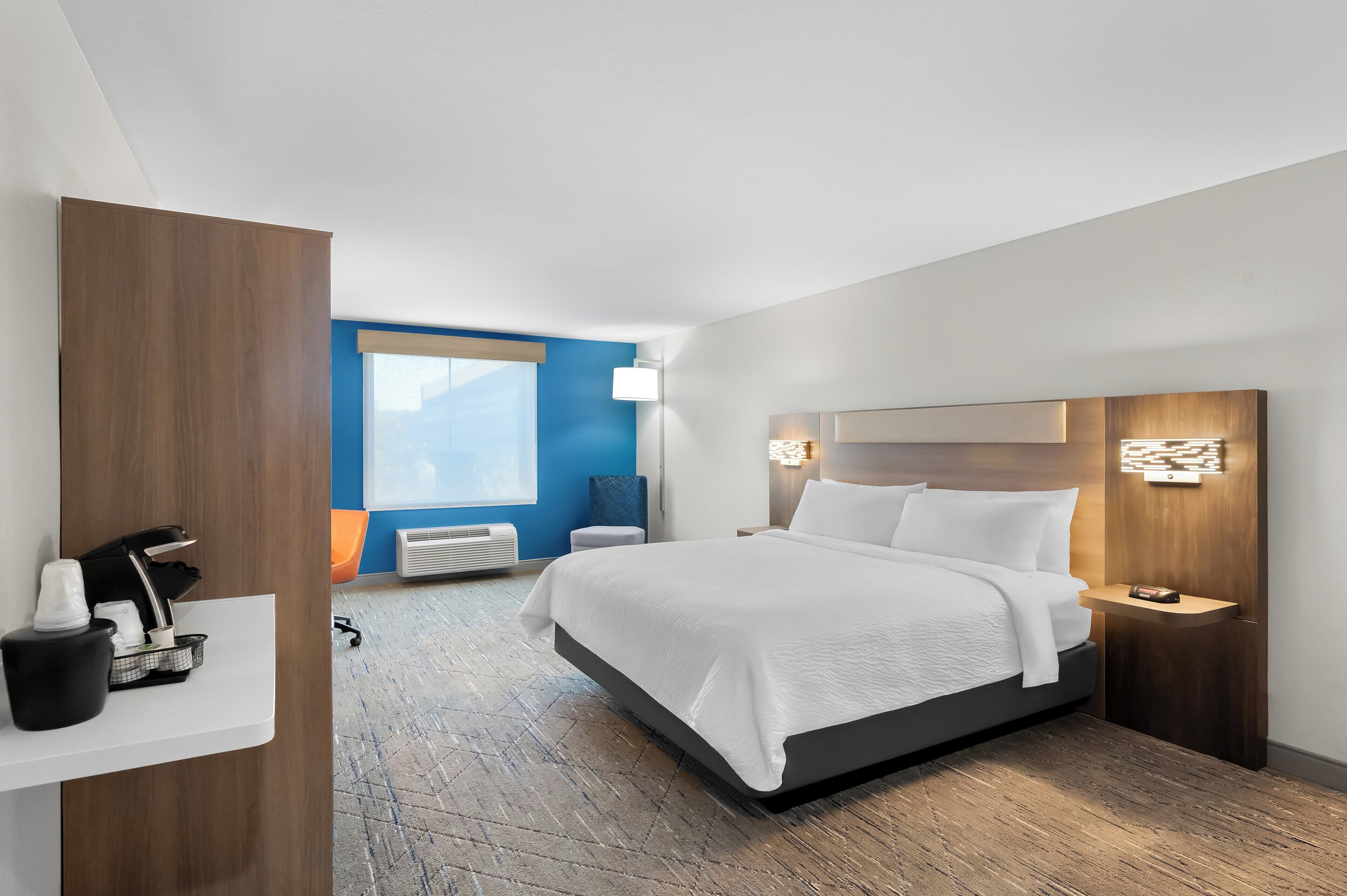 Una habitación de hotel moderna con una cama grande, mesitas de noche, un escritorio con silla y una ventana con persianas.