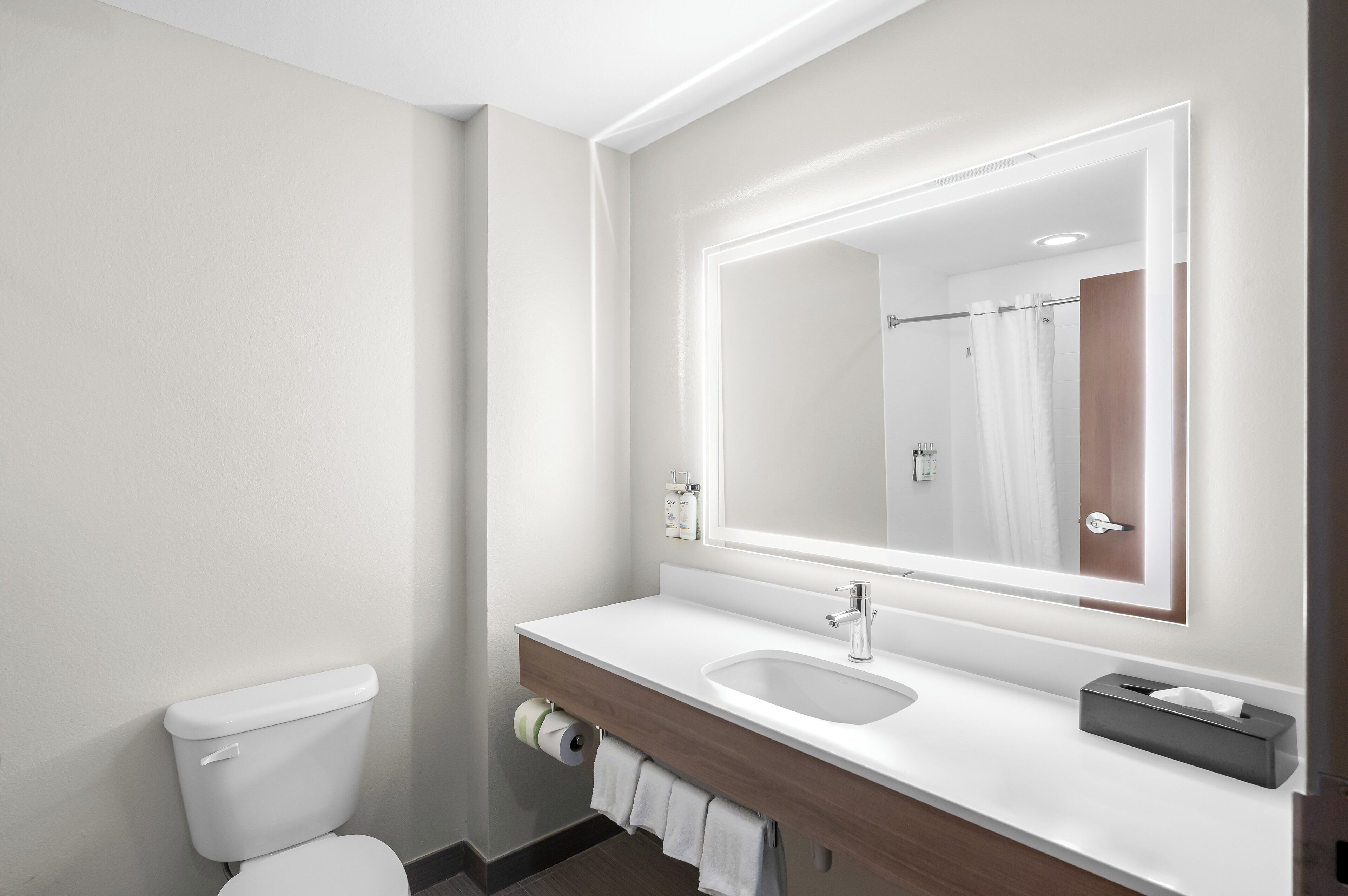 A modern bathroom with a white toilet, a sink, and a large mirror.