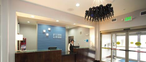 A hotel reception area with a receptionist, a Holiday Inn Express sign, an exit sign, and a check-in counter.