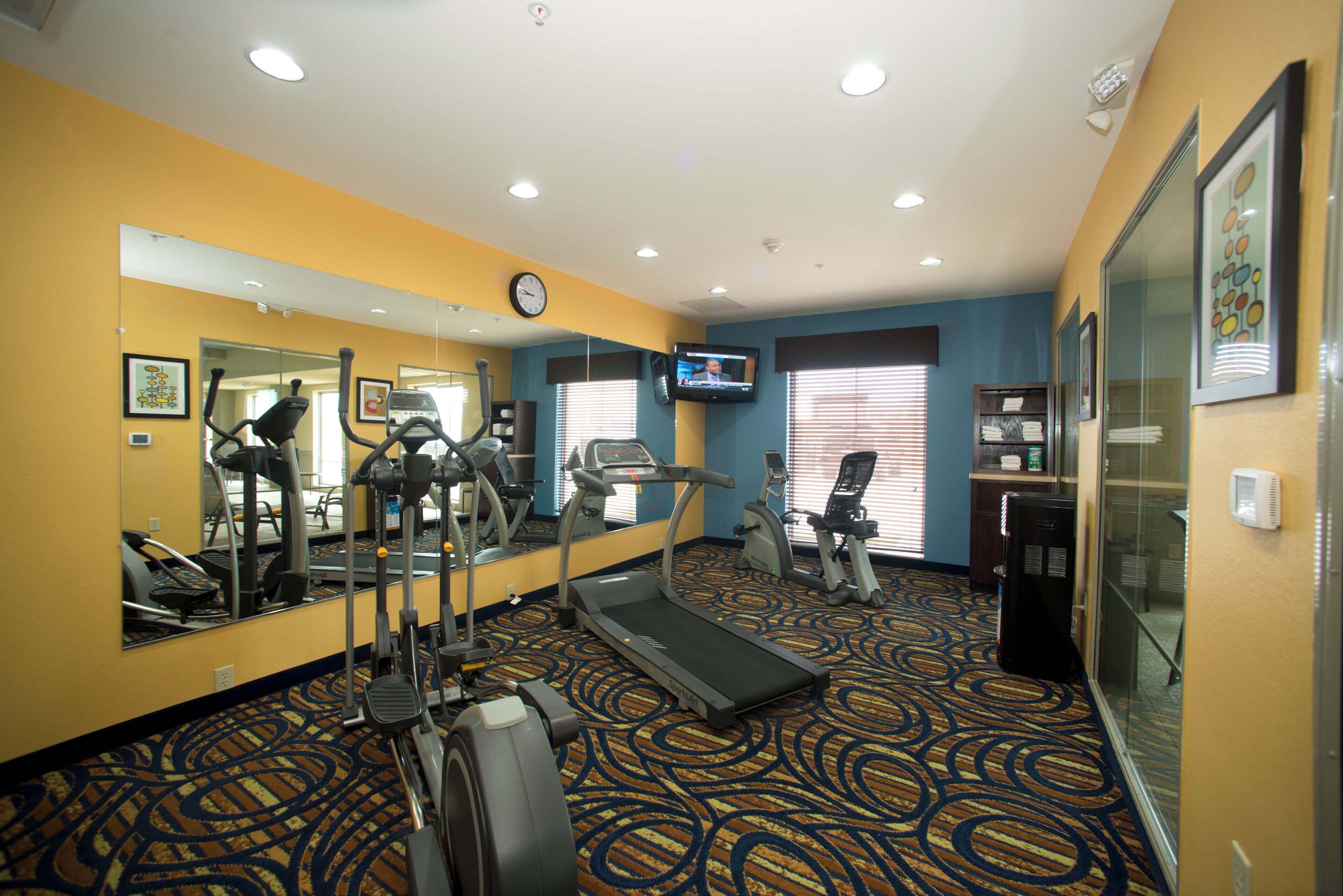 Un gimnasio de hotel con equipo de ejercicio, un televisor y un reloj en la pared.