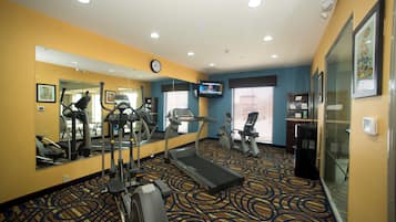 Un gimnasio de hotel con equipo de ejercicio, un televisor y un reloj en la pared.