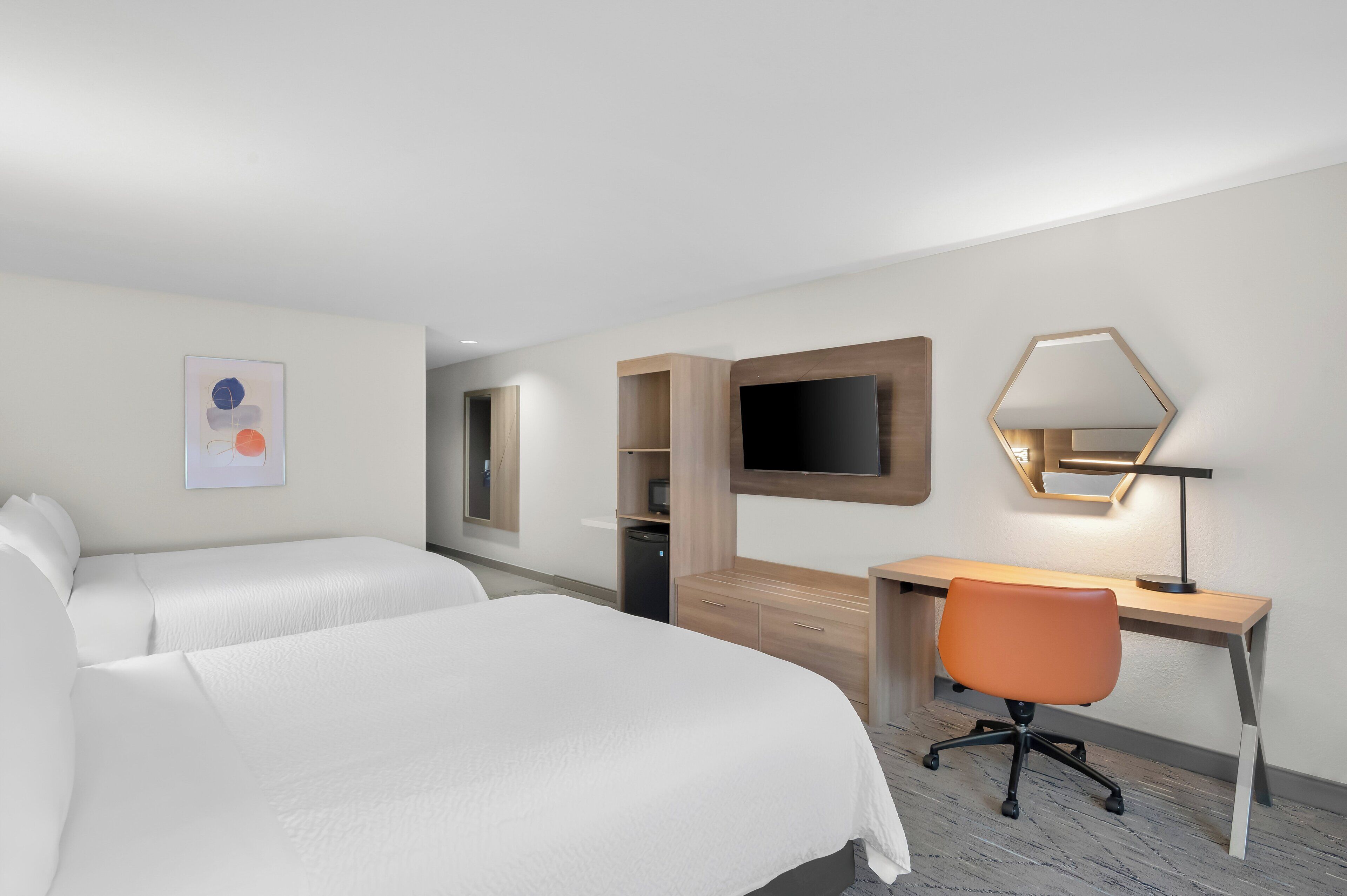 A hotel room with two beds, a desk, a chair, a TV, and a mirror.