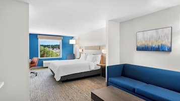 Hotellihuone, jossa on sänky, sininen sohva, pieni pöytä ja seinällä taulu.