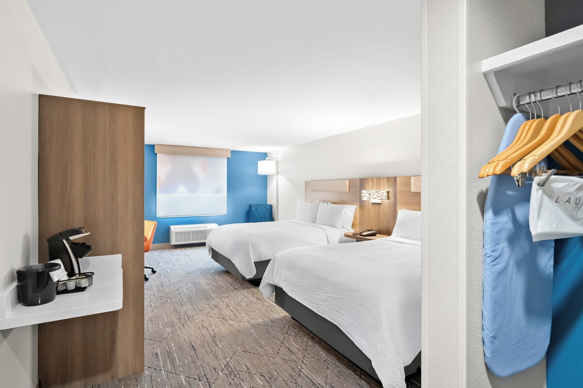 A hotel room with two beds, a coffee machine, a wardrobe, and a window with blinds.